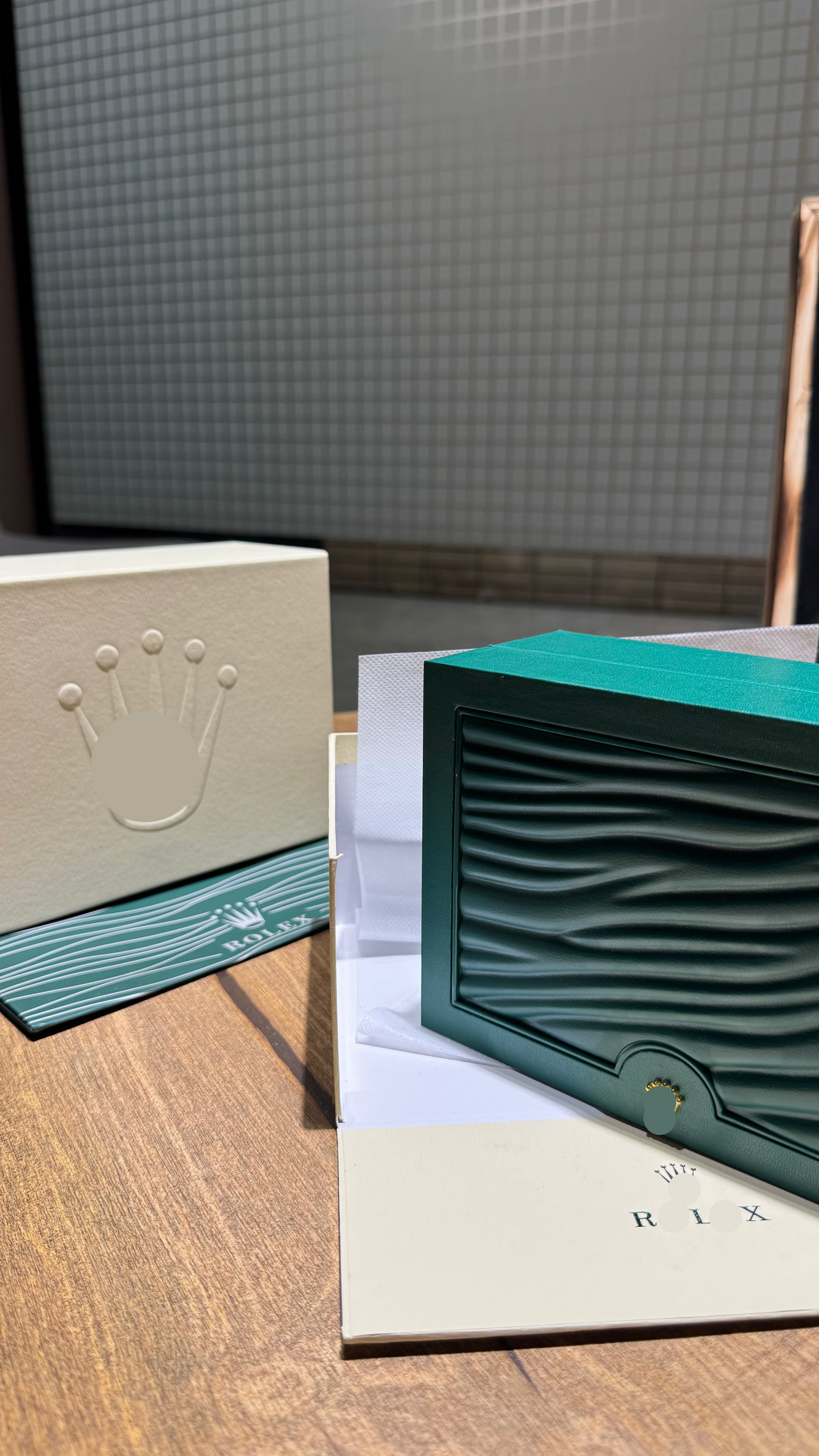 Rolex packaging including a green box and white card on a wooden surface.