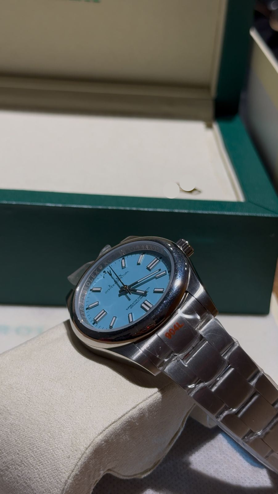 Wristwatch with blue face and silver case on a white cushion, placed inside an open green box.
